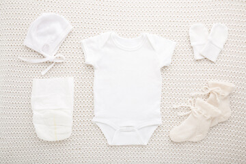Newborn bodysuit, hat, mittens, socks and diaper on light white blanket background. Closeup....