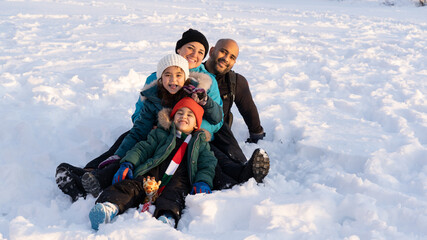 Fototapeta na wymiar four member interracial family smiling too camera sitting in the snow during sunset