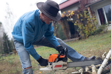 Handsome senior man working with a chainsaw during cutting trunks for firewood in his backyard.