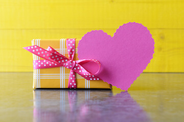 Yellow gift box and blank heart shaped card over wooden background with copy space