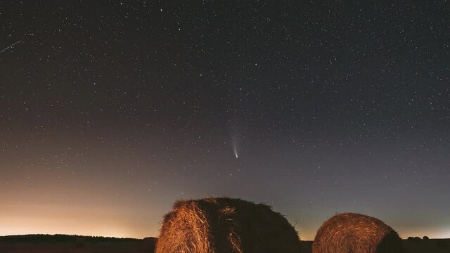 Comet Neowise C/2020 F3 In Night Starry Sky Above Haystacks In Summer Agricultural Field. Night Stars Above Rural Landscape With Hay Bales After Harvest. Agricultural Concept. 4K Timelapse