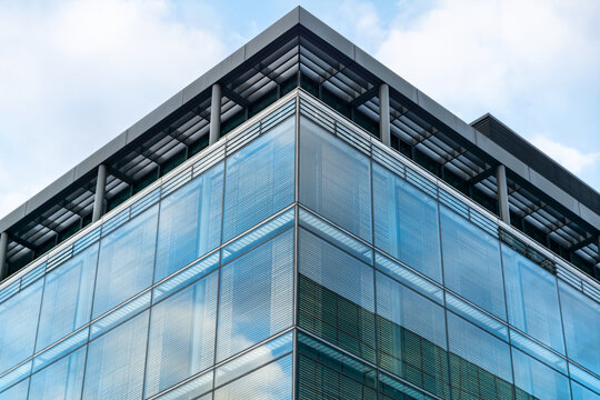Corner elevation of modern blue glass office building on a sunny day with soft blue sky and clouds above