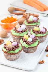 Homemade carrot cupcakes with cream cheese frosting and Easter chocolate eggs, on white plate, vertical