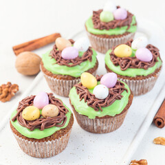 Homemade carrot cupcakes with cream cheese frosting and Easter chocolate eggs, on white plate, square format