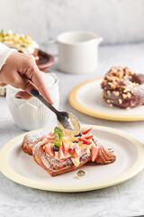 Delicious Homemade Croissant Waffle with Cream, Maple Syrup, Chopped Almond, and Strawberry. Served on Black Plate