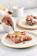 Delicious Homemade Croissant Waffle with Cream, Maple Syrup, Chopped Almond, and Strawberry. Served on Black Plate
