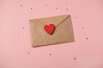 Craft envelope with the wooden heart and little golden stars on the rose background. Flat lay, top view. Romantic love letter for Valentine's day concept.