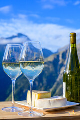 Tasty cheese and wine from Savoy region in France,  tomme and reblochon de savoie cheeses and glass of white wine served outdoor with Alpine mountains peaks on background