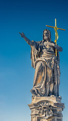 Statue of saint with cross at the Charles Bridge in Prague at blue gradient sky, Czech Republic, summer time