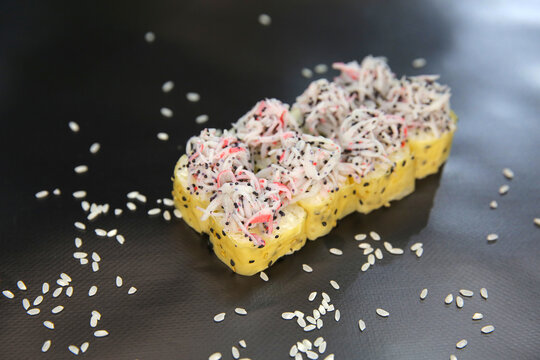 Side view of Japanese sushi roll wrapped in mamenori seaweed with black, white sesames with crab meat sticks and flying fish roe Tobiko on top isolated on black background with scattered sesame seeds

