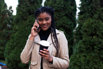 happy african american woman on the street with phone and coffee