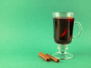 Glass of mulled wine and cinnamon sticks on a mint-colored background. Hot beverage for winter time