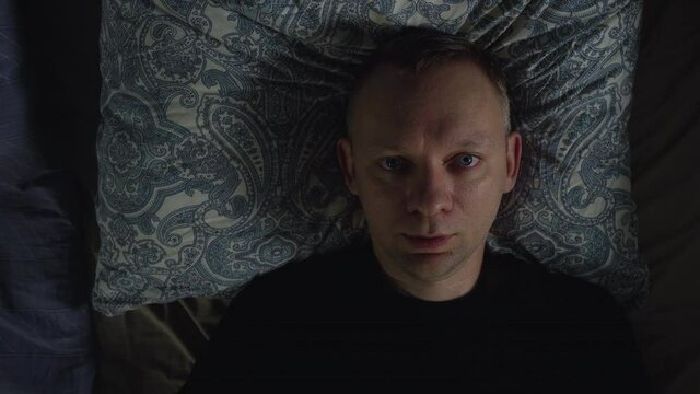 Calm handsome man goes to sleep in comfortable cozy fresh bed enjoying healthy good sleep at night
