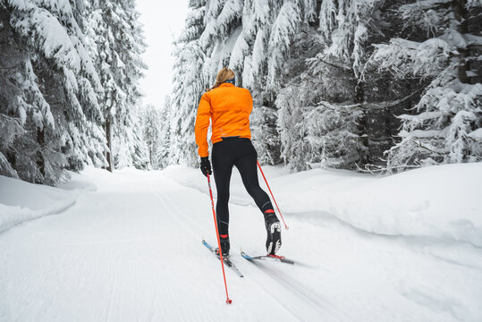 Langl&auml;ufer von hinten mit orangener Jacke auf der Loipe im Winter