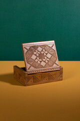 An old vintage handcarved wooden box in a dark brown color opened up on a yellow surface with a green background. An antique authentic handmade woodcarved treasure container