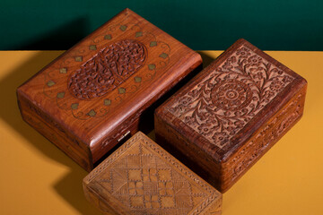 Fototapeta premium Old vintage handcarved wooden boxes in dark brown colors on a yellow surface with a green background. A collection of authentic handmade woodcarved treasure containers in different sizes