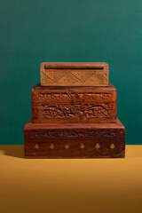 Old vintage handcarved wooden boxes in dark brown colors piled up on a yellow surface with a green background. A collection of authentic handmade woodcarved treasure containers in different sizes.
