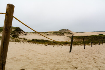 Lacka sand dune with rope fence on the foreground and grey misty plain sky