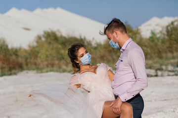 Young loving couple in medical masks in park during quarantine on wedding day.