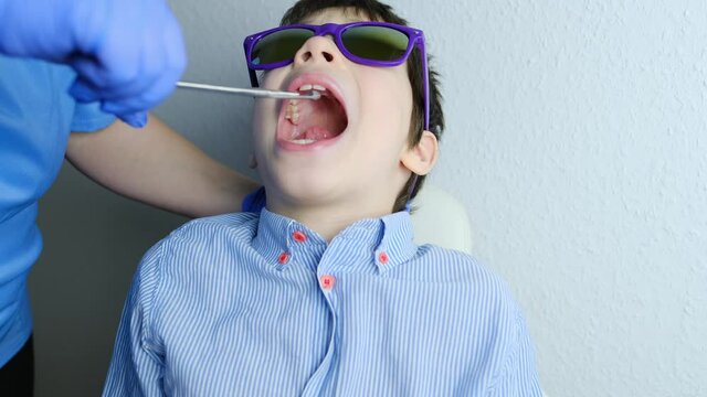 doctor examines oral cavity of small patient, molars grow, length of frenum of the tongue, boy, kid with open mouth, close up of child&rsquo;s teeth