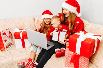 mother and two small children in Santa Claus hats, are having a Christmas party, video conference...