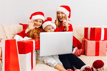 mother and two small children in Santa Claus hats, are having a Christmas party, video conference...