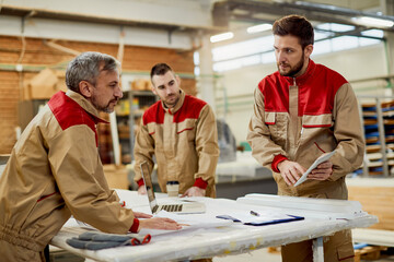 Group of carpenters cooperating while using touchpad in a workshop.