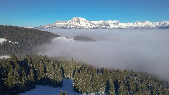 Winter mountain landscape with snow covered white peaks and fir tree forest, aerial 4k video footage from drone, scenic panorama from Meg&egrave;ve with sea of clouds near Chamonix, France
