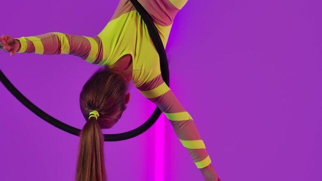 An acrobatic performance on an air hoop performed by a young circus performer. Teenager girl in a yellow leotard rotates under the dome. Close up. Slow motion.