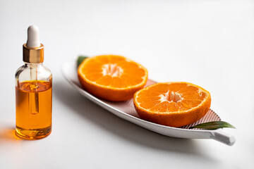 A bottle of aromatic tangerine oil and two halves of a cut tangerine on a white background.