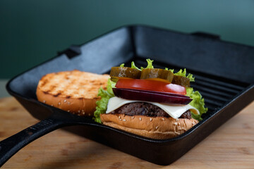 A delicious burger next to a fluted frying pan. A chef's knife. Lots of vegetables.