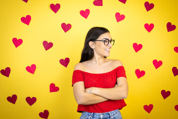 Young beautiful woman over yellow background with red hearts looking to side, relax profile pose with natural face and confident smile.