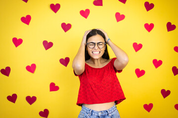 Young beautiful woman over yellow background with red hearts suffering from headache desperate and stressed because pain and migraine with her hands on head