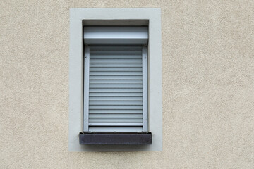 Bright brick wall with small window and closed  aluminum shutter, jalousie rolled up symbol for lockdown, no person