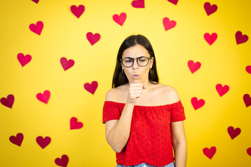 Young beautiful woman over yellow background with red hearts with her hand to her mouth because she's coughing