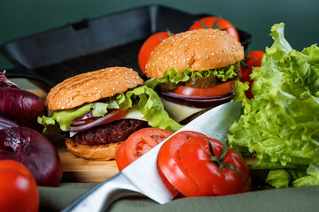 A delicious burger next to a fluted skillet. A chef's knife. Lots of vegetables.