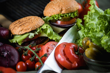 A delicious burger next to a fluted skillet. A chef's knife. Lots of vegetables.