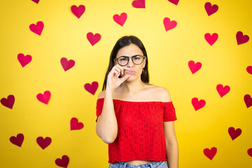 Young beautiful woman over yellow background with red hearts mouth and lips shut as zip with fingers. Secret and silent, taboo talking