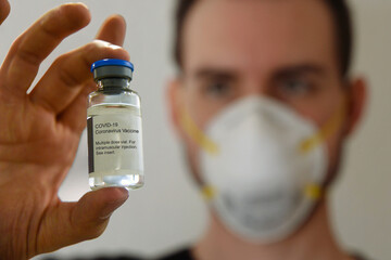 A man wearing a protective N95 respirator mask holds a COVID-19 coronavirus vaccine vial.