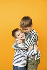 Yellow background studio photograph of little cute toddler siblings hugging each other. Brothers...