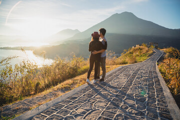 Hispanic couple watching the sunrise in Lake Atitlan - traveling couple embracing at the top of the...