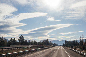 Beautiful landscape on a sunny day, a highway among the mountains, in front of high mountains in clouds and fog, cars and trucks are driving along the road. Montana, USA, 11-23-2019