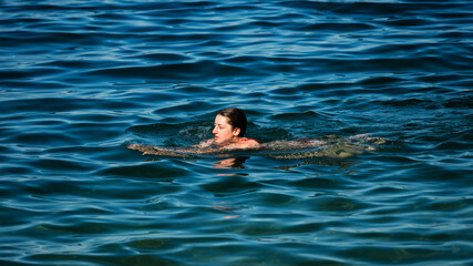 A young girl swims in the crystal clear water of a mountain lake.