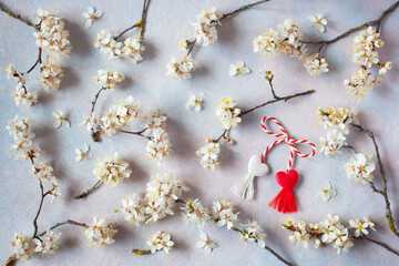 Decorative background with flowering branches of cherry plum and red and white symbol of the martenitsa of the holiday of the arrival of spring.