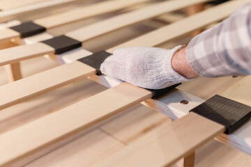 Male worker's hand in glove assembling bed, connecting slats to bed frame