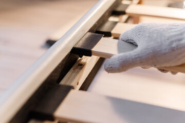Male worker's hand in glove assembling bed, connecting slats to bed frame