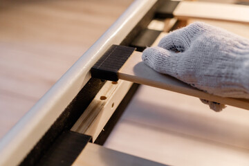 Male worker's hand in glove assembling bed, connecting slats to bed frame