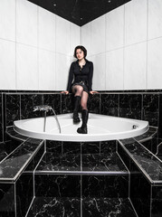 A young girl in high leather boots and a short leather skirt poses in a chic black and white bathroom.