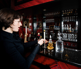 A young girl, dressed in a gothic style, poses in a posh alcoholic bar in red and black colors.