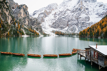 snowy landscape with mountains, trees, boats to navigate in the water in the lago di braies. Located in the dolomites, the Italian alps